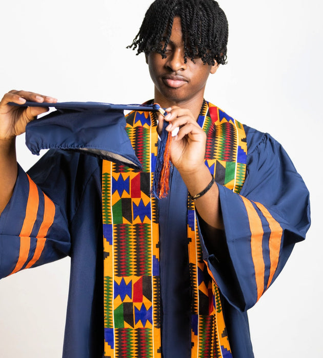 Student wearing graduation gown, holding graduation cap, wearing Kente Print sash